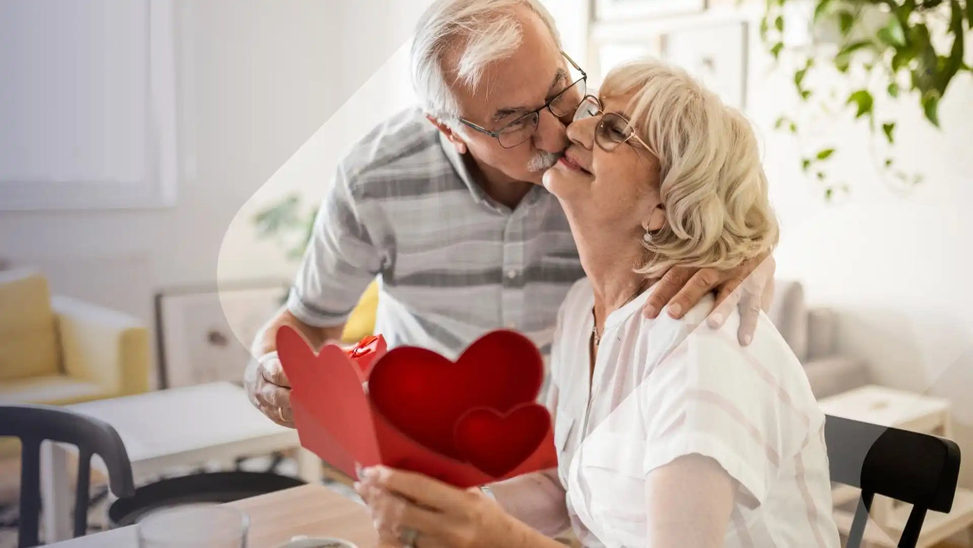 Älteres Paar, das einen Kuss teilt, mit einer roten herzförmigen Karte im Vordergrund.