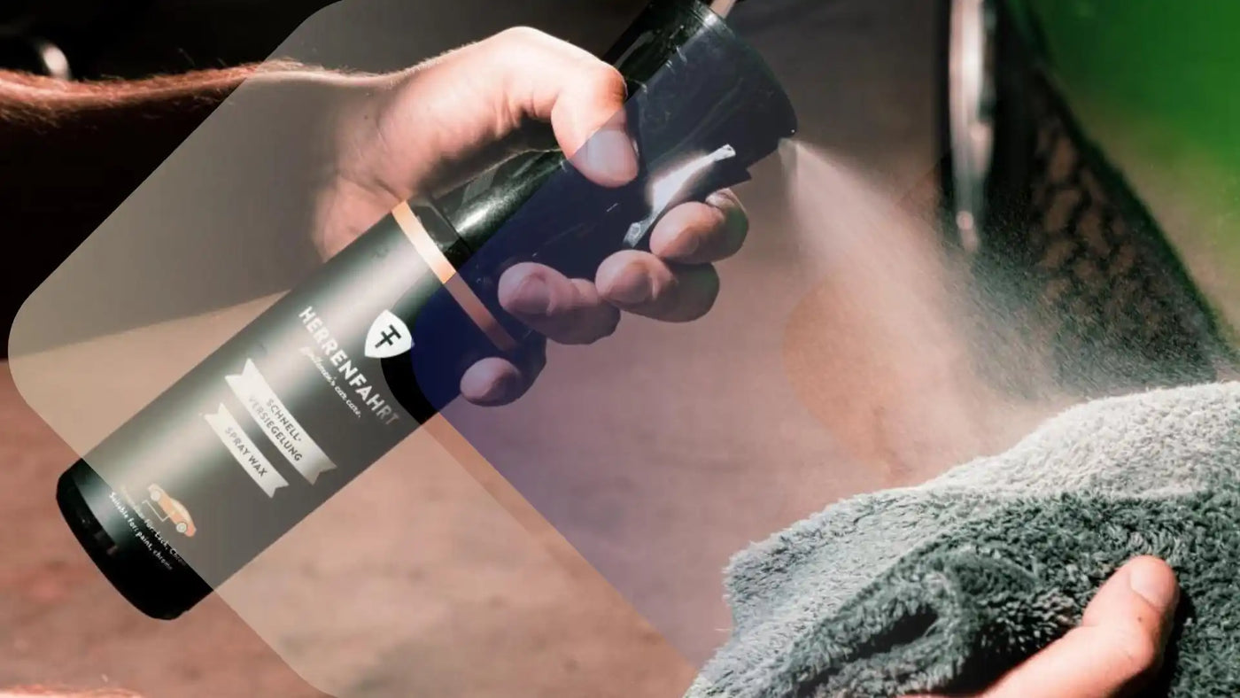 Eine schwarze Sprühflasche mit der Aufschrift »HERRENFAHRT« und einem goldenen und weißen Etikett, die einen feinen Nebel auf ein graues Mikrofaserhandtuch sprüht.